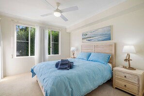 Ein Schlafzimmer mit einem Bett, zwei Nachttischen, einem Deckenventilator und einem Fenster mit Vorhängen.