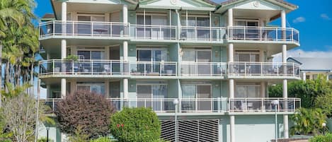 A multi-story residential building with balconies, a garage, and a landscaped garden.