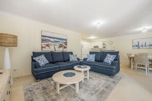 Ein Wohnzimmer mit einer Eckcouch, zwei runden Couchtischen, einem Essbereich mit Tisch und Stühlen sowie Kunstwerken an den Wänden.