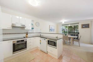 Eine moderne Küche mit weißen Schränken, einem Backofen, einer Mikrowelle und einem Geschirrspüler. Es gibt einen Essbereich mit Tisch und Stühlen sowie einen Balkon mit Blick.