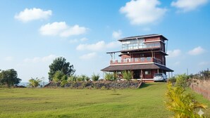 A two-story house with a balcony, a car parked in front, and a grassy field in the background.