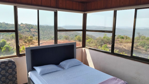 A bedroom with a bed, a chair, and large windows offering a view of a hilly landscape.