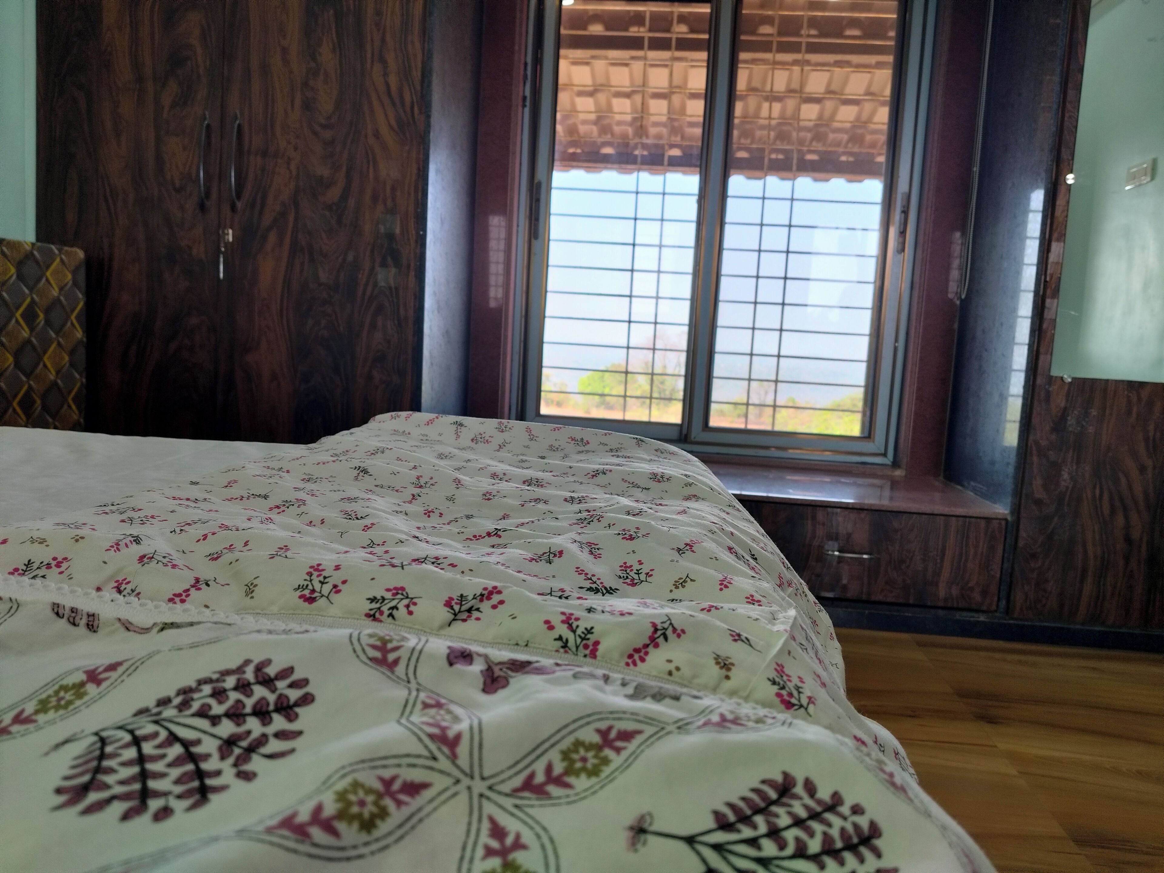 A bedroom with a bed, wooden wardrobe, and a window with a view.