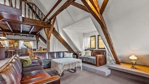 A loft-style living room with exposed wooden beams, a leather sofa, a patterned ottoman, and a dining area with wooden chairs. - Family-Friendly Apartment Close to Nature & Hiking Trails (Meinerzhagen)