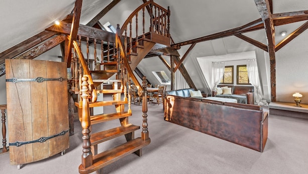 A loft bedroom with exposed wooden beams, a wooden ladder, a large trunk, and a leather sofa. - Family-Friendly Apartment Close to Nature & Hiking Trails (Meinerzhagen)