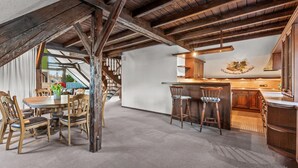 A rustic interior with exposed wooden beams, a dining area with wooden chairs and a table, and a kitchen with wooden cabinets and a bar area. - Family-Friendly Apartment Close to Nature & Hiking Trails (Meinerzhagen)