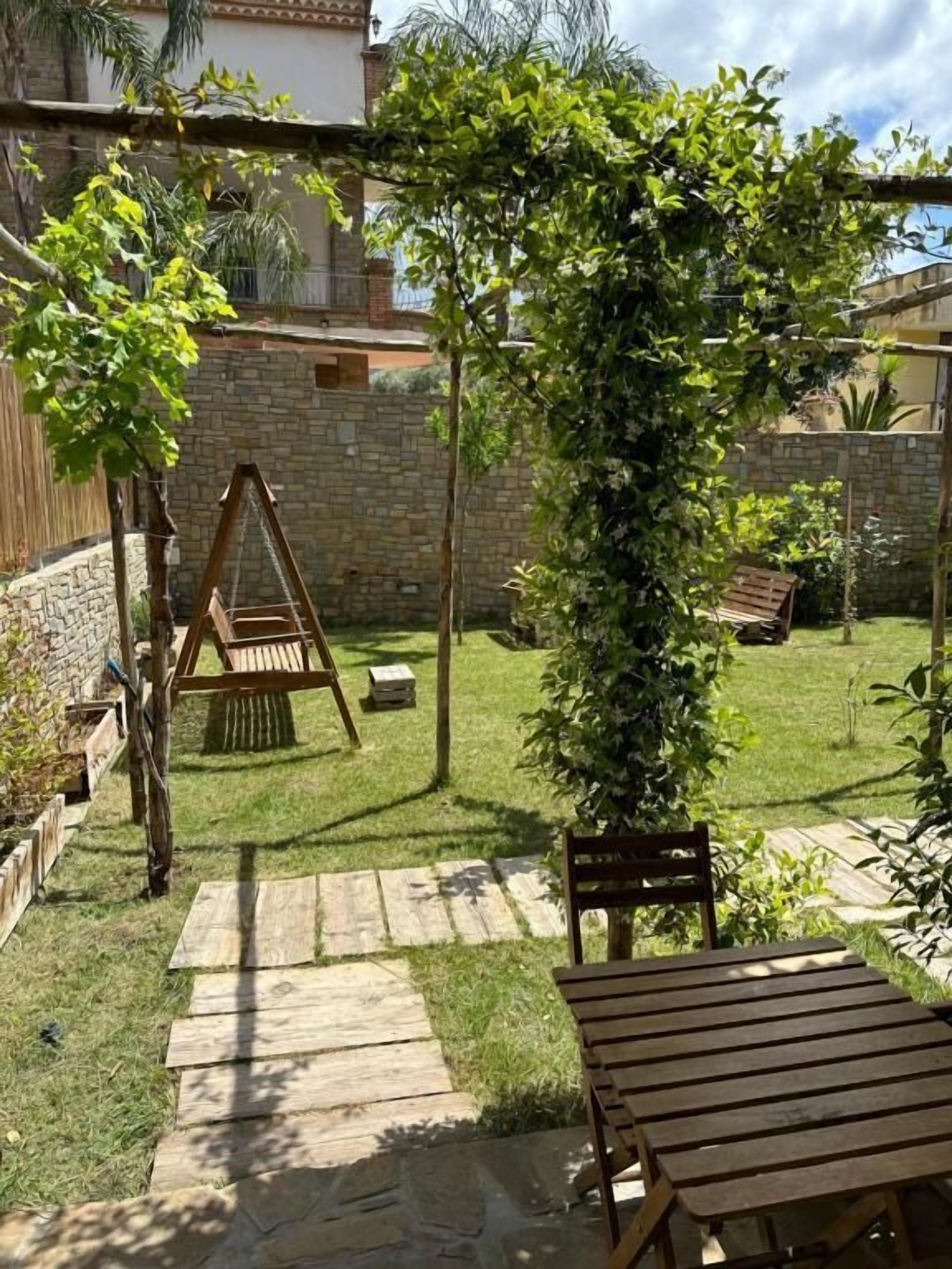 A patio with a swing set, wooden table, and a pergola covered in climbing plants.