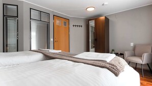 Ett hotellrum med två sängar, en trädörr, en stol och ett litet bord med en växt.