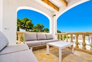 A balcony with a white sofa, a small table, and a stone floor. - Villa Irenal Javea, with Air Conditioning and Private Pool (Javea)