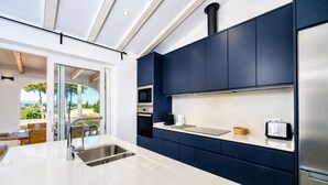Una cocina moderna con armarios azul oscuro, electrodomésticos de acero inoxidable y un amplio ventanal con vistas a un paisaje.