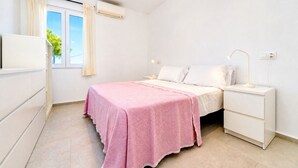 Un dormitorio con cama, mesitas de noche, cortinas en la ventana y un equipo de aire acondicionado.