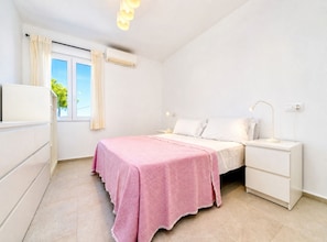 A bedroom with a bed, bedside tables, a nightstand, a window with curtains, and an air conditioning unit. - Villa Irenal Javea, with Air Conditioning and Private Pool (Javea)
