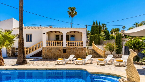 Una piscina con borde de piedra, una palmera y un edificio con balcón.