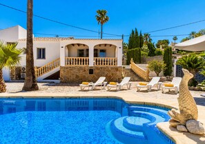 A swimming pool with a stone border, a palm tree, and a building with a balcony. - Villa Irenal Javea, with Air Conditioning and Private Pool (Javea)