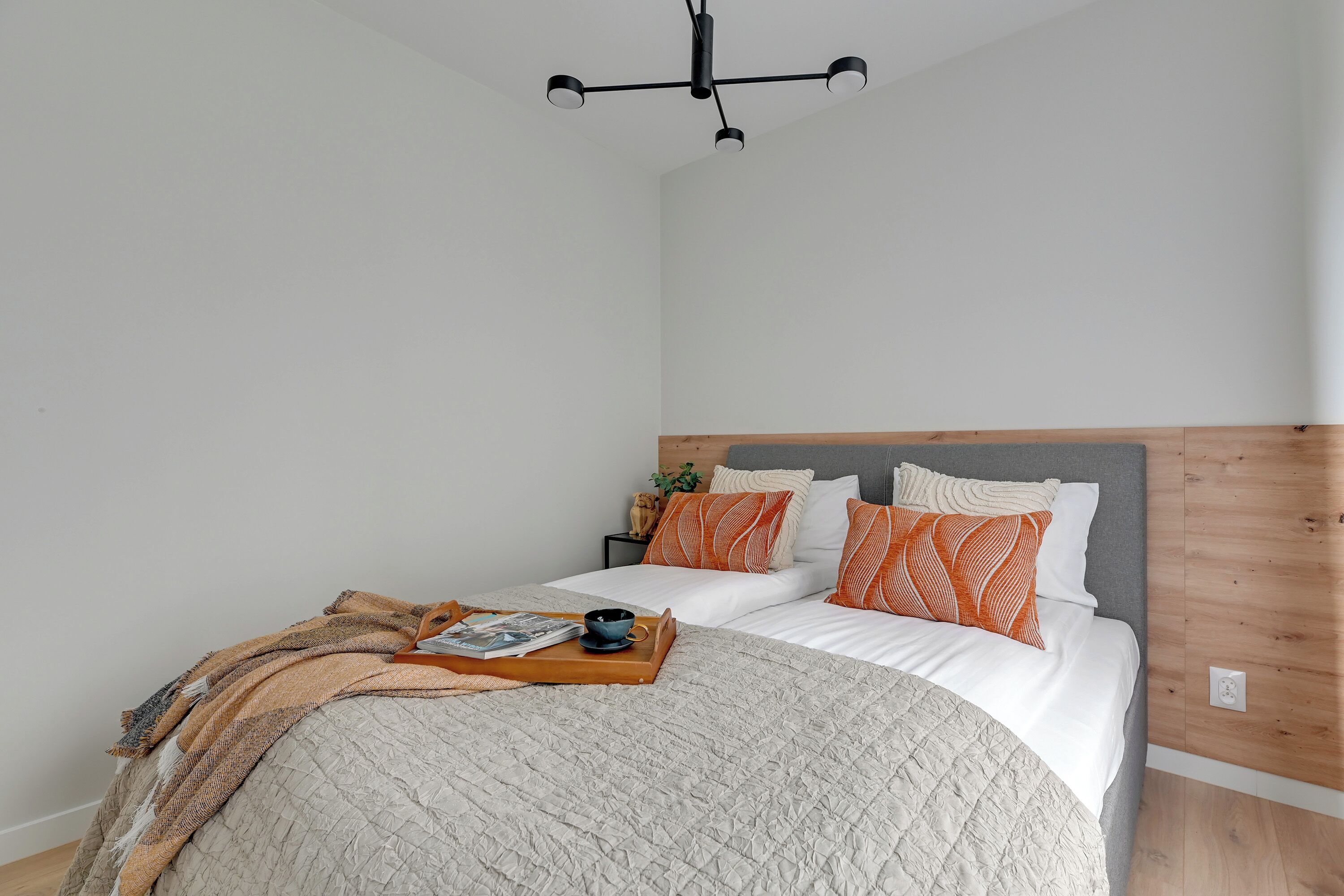 Un lit bien fait, avec une tête de lit en bois, une tablette sur laquelle reposent une tasse et un magazine, et un luminaire suspendu.
