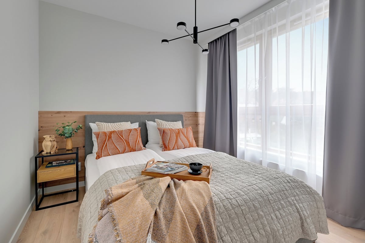 Un dormitorio moderno con una cama, mesitas de noche, una lámpara colgante y una ventana con cortinas.