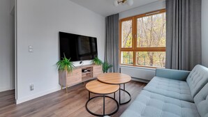 A modern living room with a sofa, two round tables, a TV, and a window with curtains. - Młoda Polska Apartments with parking  (Sopot)