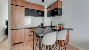 A modern kitchen with wooden cabinetry, a black countertop, and a dining area with two chairs. - Młoda Polska Apartments with parking  (Sopot)