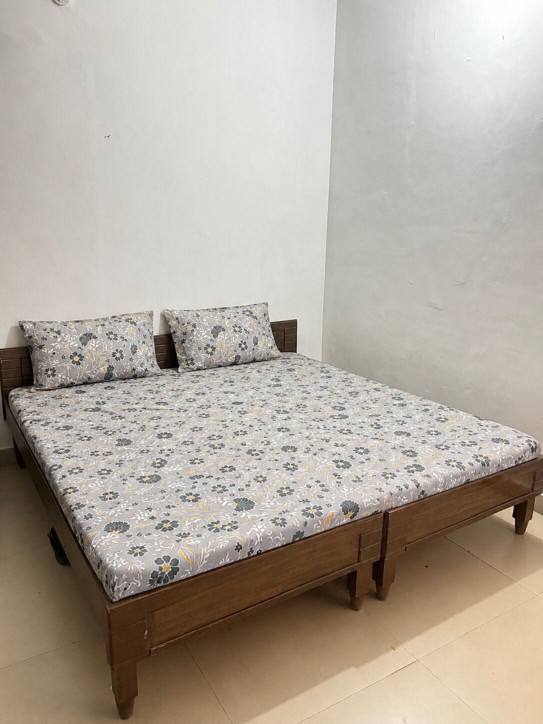 Un llit amb un llençol estampat floral, un capçal de fusta i dos coixins.