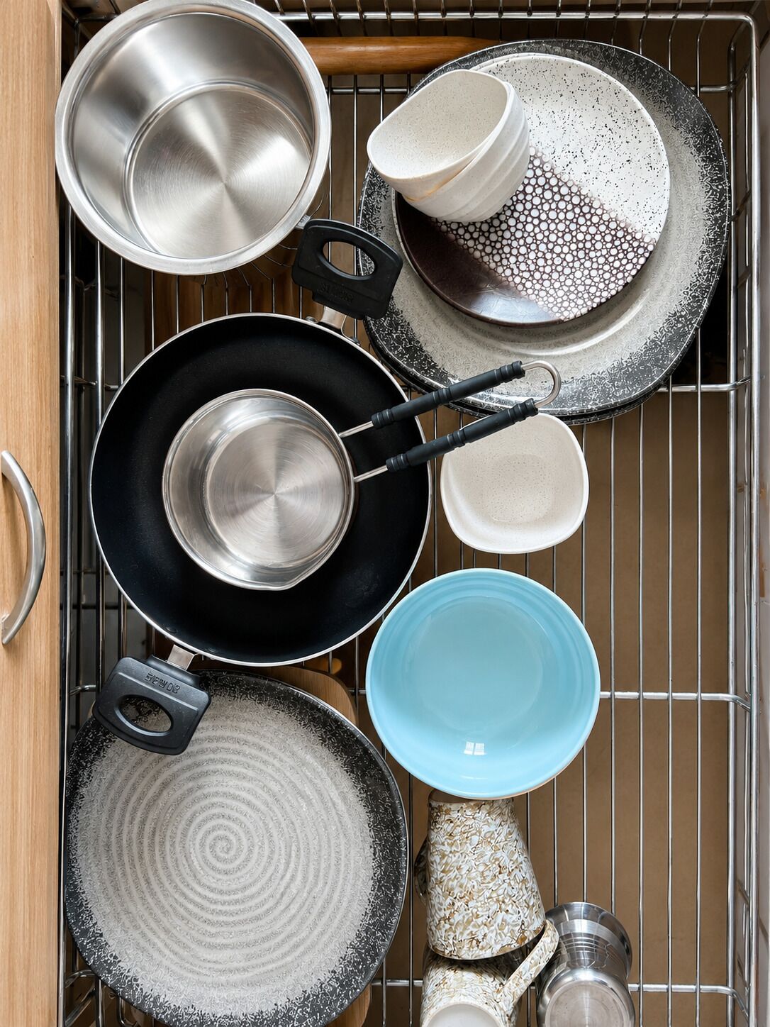 A kitchen with various cookware and dishes, including pots, pans, and plates, arranged on a rack.