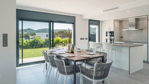 A modern kitchen with a dining area, large windows, and a view of the outdoors. - Villa Cala Prona : Private Mediterranean Retreat (Girona)