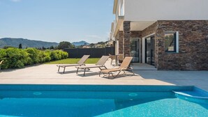 A swimming pool with lounge chairs, a stone facade, and a view of distant hills. - Villa Cala Prona : Private Mediterranean Retreat (Girona)