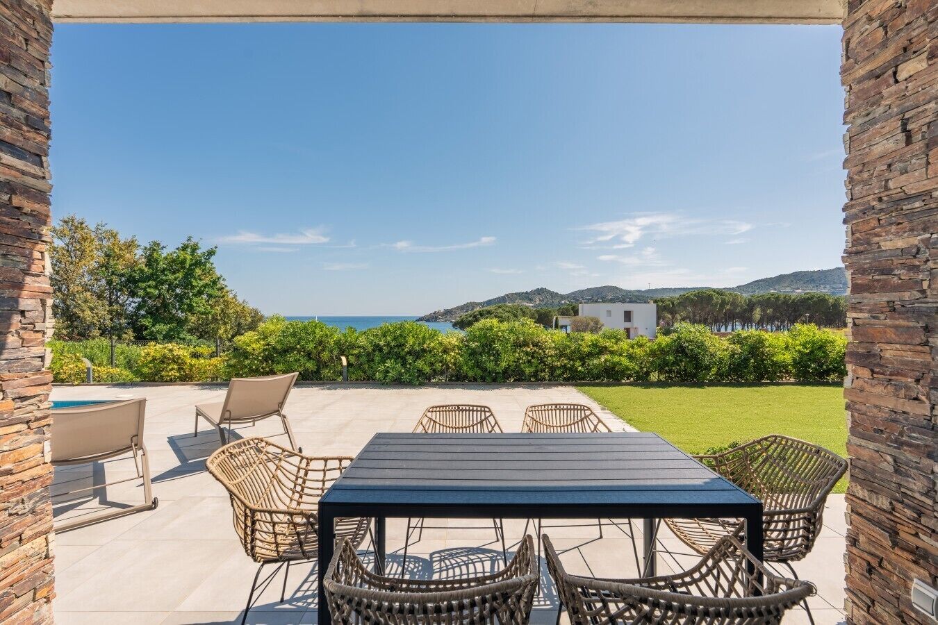 Un patio exterior con una mesa y sillas, una piscina y vistas al mar y las colinas.