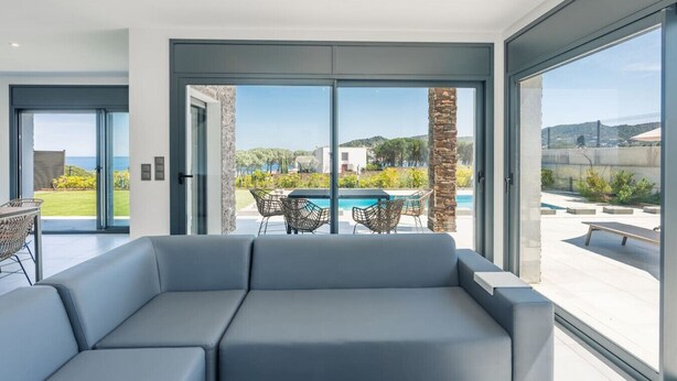 Un salon moderne dot é d’un grand canapé, d’un coin repas avec des chaises, et offrant une vue sur une piscine et un jardin.