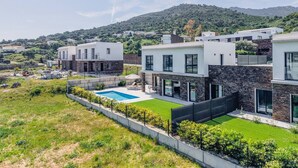 Un complexe résidentiel moderne comprenant plusieurs maisons, une piscine et un paysage vallonné en arrière-plan.