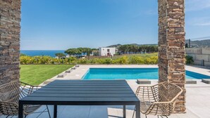 Un espace aménagé au bord de la piscine, avec vue sur la mer, un bâtiment blanc et un pilier en pierre.