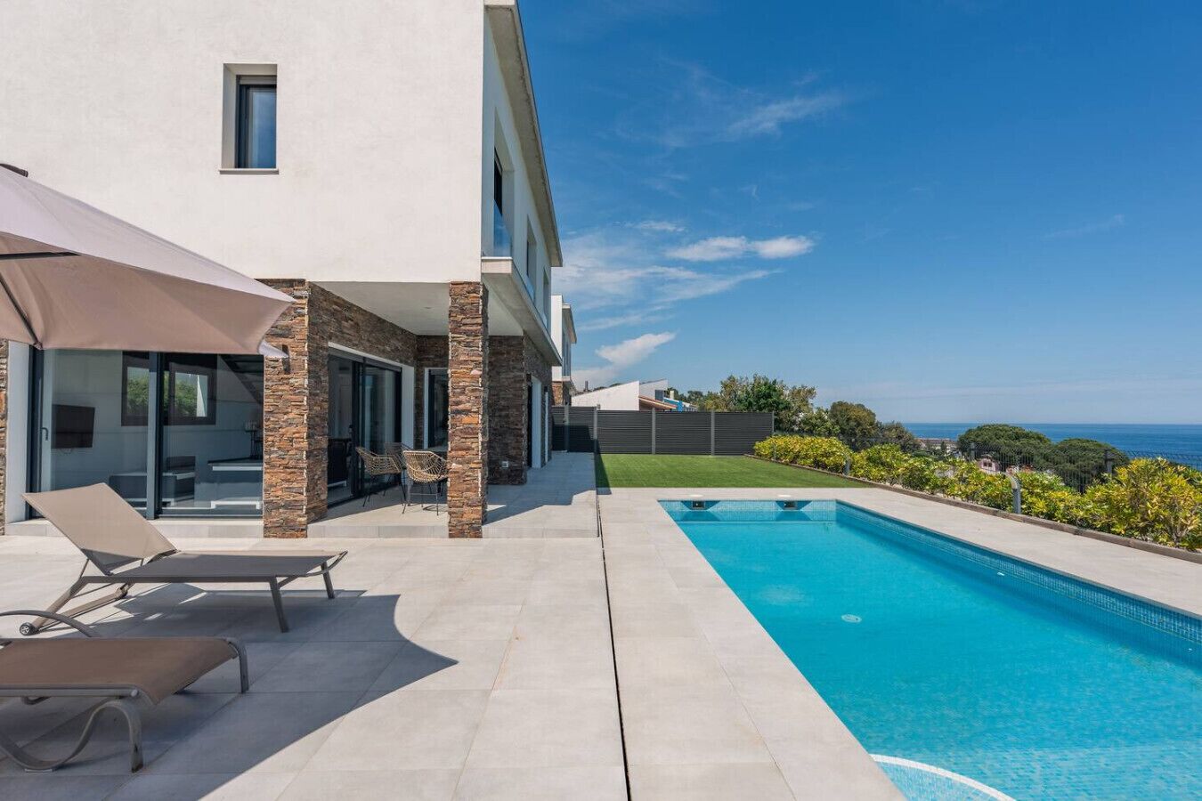 A modern house with a swimming pool, outdoor seating, and a view of the sea.