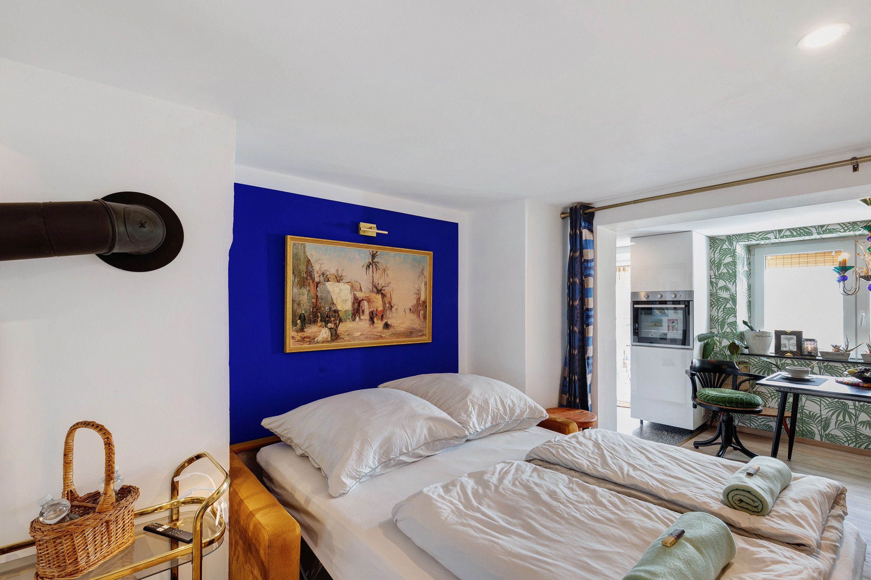 Habitación de hotel con cama, un cuadro en la pared, kitchenette y baño visible a través de una puerta abierta.