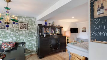 Une pièce chaleureuse avec un plancher en bois, une armoire noire aux portes en verre, un lit avec une tête de lit blanche et un mur recouvert d’un tableau noir.