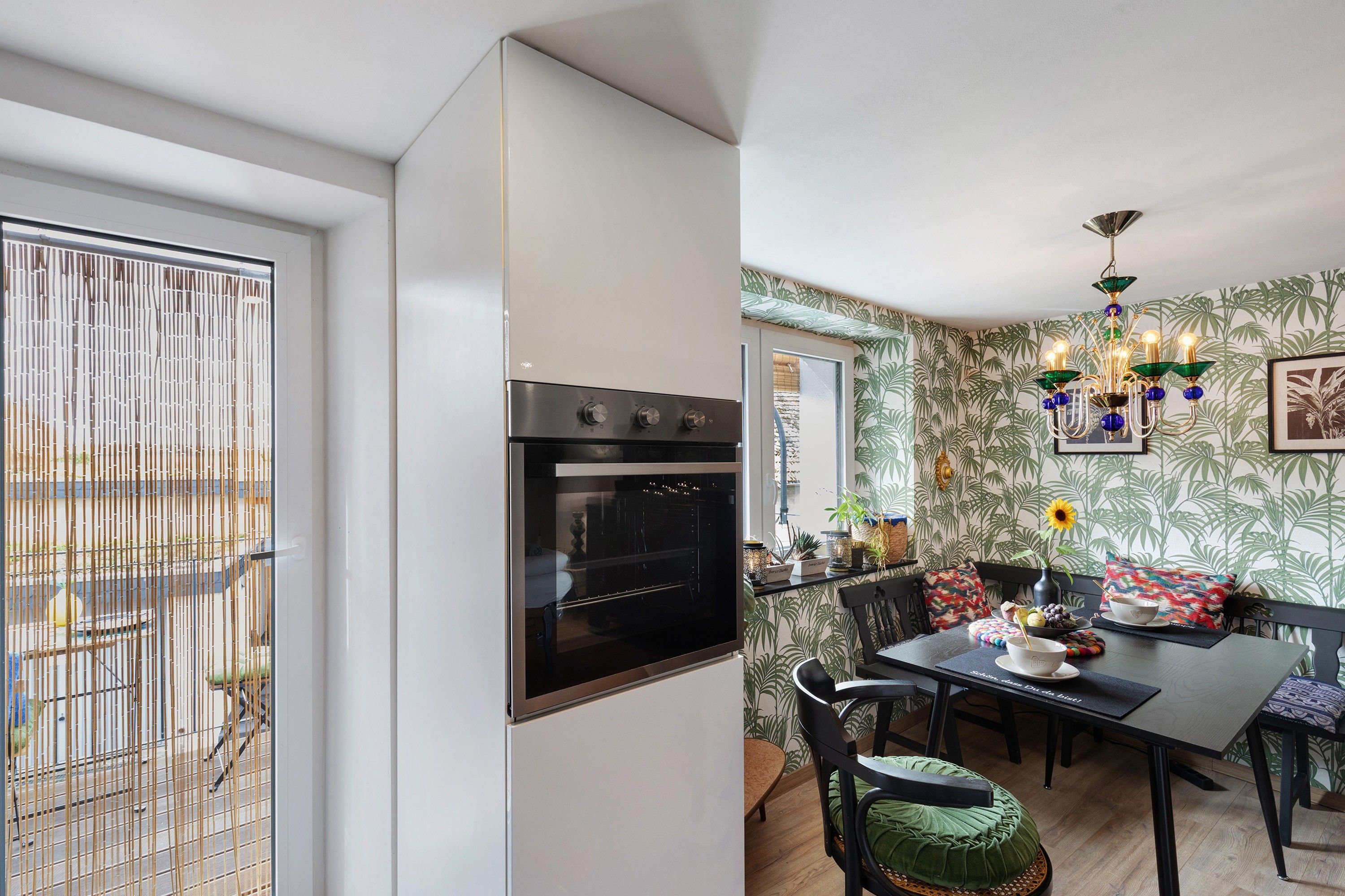 A modern kitchen with a built-in oven, a dining area with a table and chairs, and a decorative chandelier.