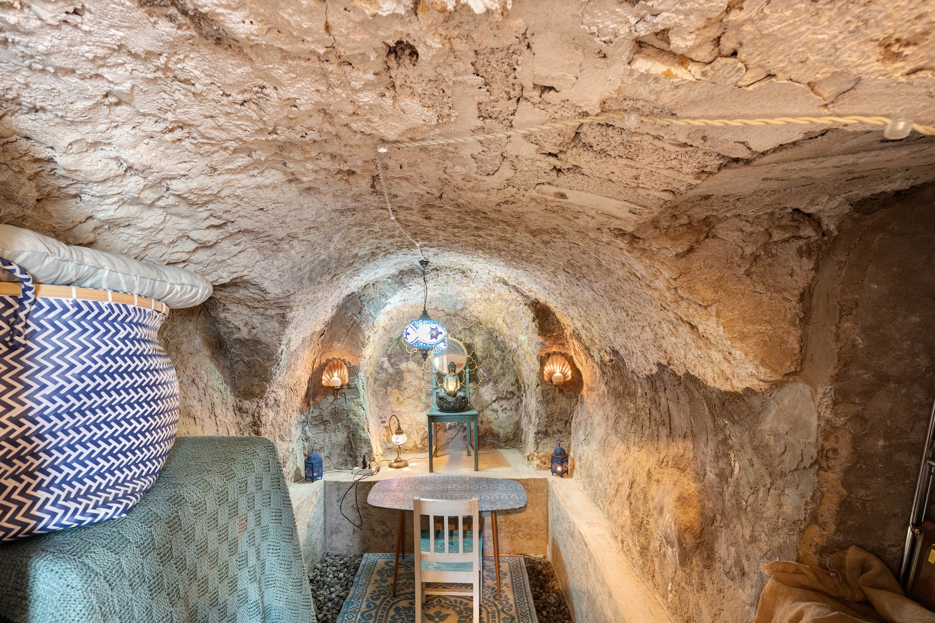 A cave-like interior with a table and chairs, a hanging lamp, and a decorative Buddha statue.