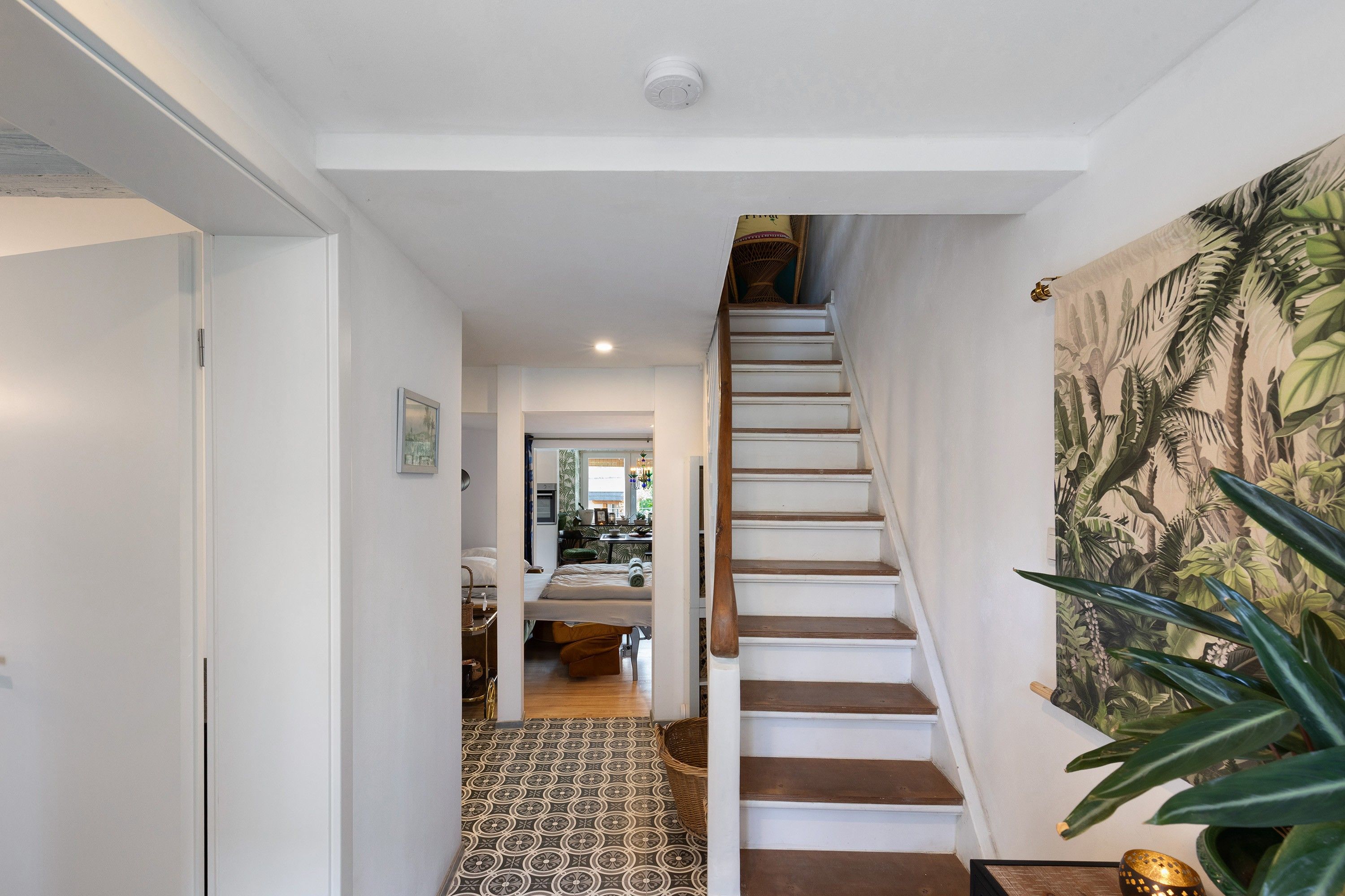A staircase with a patterned floor leading to a room with a bed and a desk.