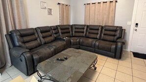 En stue med en hjørnesofa, et sofabord i glas og gardiner.