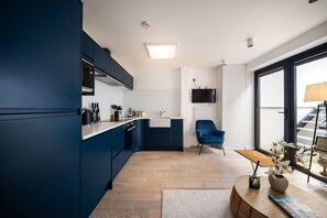 A modern kitchen with dark blue cabinets, a white countertop, and a wooden floor. There is a blue chair, a TV mounted on the wall, and a window with a view of the outside. - 1 Min Walk to Euston Station Modern Apartment (London)