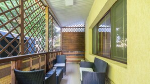 Un patio cubierto con mobiliario de mimbre, un banco de madera y un ventanal grande.