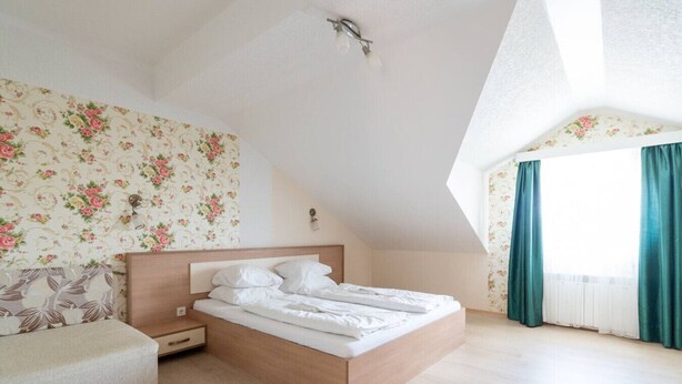 A bedroom with a bed, a nightstand, a sofa, a window with curtains, and a skylight. - FarawayHomes Aparthotel Vienna Airport #8 (Bruck an der Leitha)