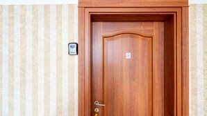 A wooden door with a number 8, a keyhole, and a doorbell on a striped wall. - FarawayHomes Aparthotel Vienna Airport #8 (Bruck an der Leitha)