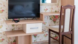 A bedroom with a TV, a wooden cabinet, a mirror, and a floral wallpaper. - FarawayHomes Aparthotel Vienna Airport #10 (Bruck an der Leitha)