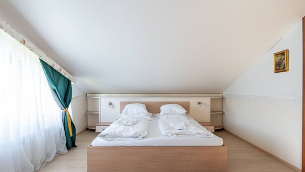 A bedroom with a bed, a dresser, a nightstand, and a window with curtains. - FarawayHomes Aparthotel Vienna Airport #10 (Bruck an der Leitha)