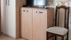 A room with a wardrobe, a television on a cabinet, a chair, and floral wallpaper. - FarawayHomes Aparthotel Vienna Airport #1 (Bruck an der Leitha)