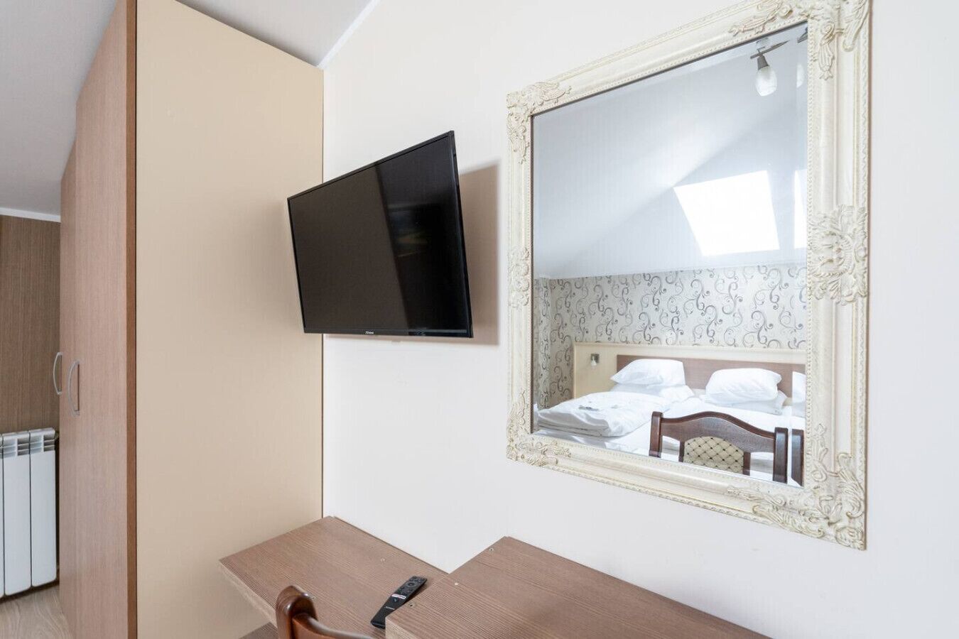 Una camera d'albergo con un letto, una televisione a muro, una scrivania in legno e uno specchio con cornice decorata.