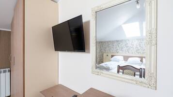 Una camera d'albergo con un letto, una televisione a muro, una scrivania in legno e uno specchio con cornice decorata.