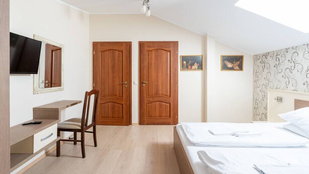 Un dormitorio con una cama, un escritorio, una silla, dos puertas de madera, un televisor y obras de arte en la pared.