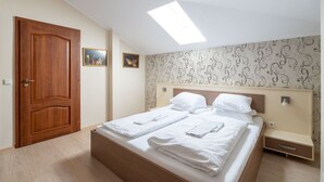 Un dormitorio con puerta de madera, cama con ropa blanca, tragaluz y papel tapiz estampado.