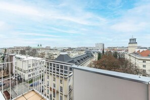 Ein Hochhaus mit mehreren Etagen, einem Balkon und Blick auf eine Stadtlandschaft mit verschiedenen Gebäuden und einem Turm.