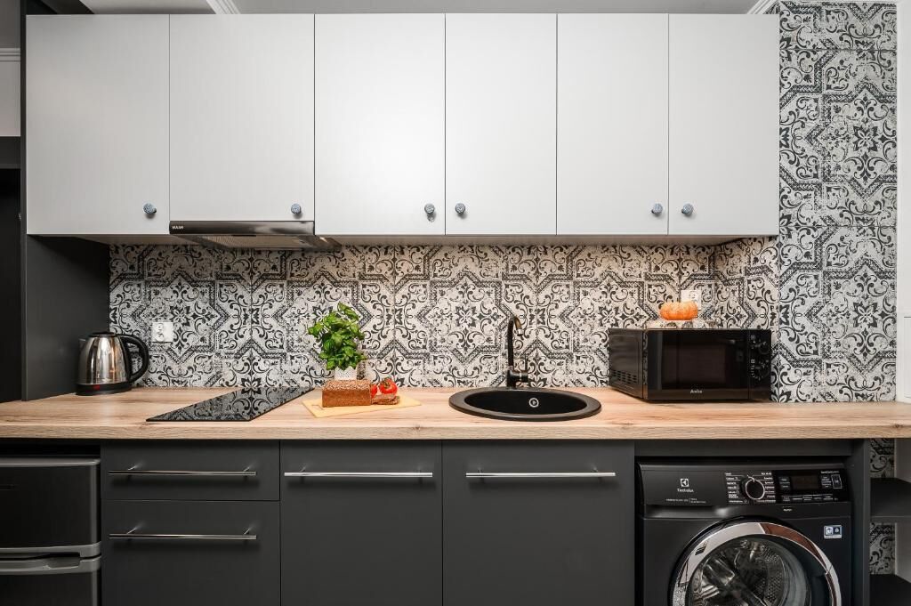 A kitchen with white cabinets, a patterned backsplash, a microwave, a sink, and a washing machine.